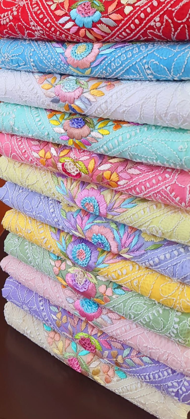 Stack of colorful Lucknowi Chikankari embroidered fabrics with intricate floral handwork.