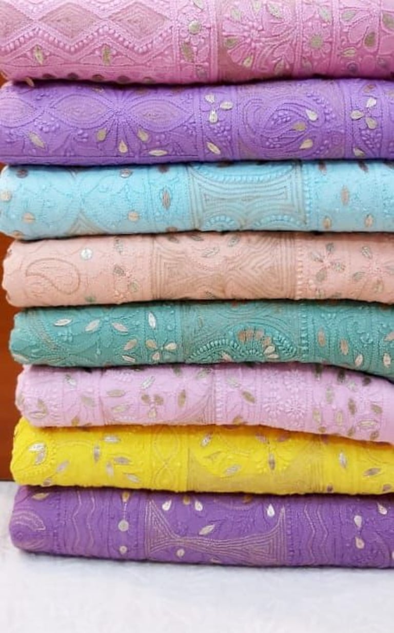 Stack of colorful Chikankari embroidered fabrics with sequins in pastel pink, blue, and yellow.