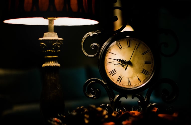 Vintage ornamental table clock with Roman numerals illuminated by a warm lamp in a dark room.