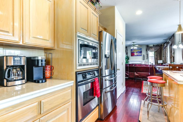 Modern kitchen with light oak cabinets, stainless steel appliances, and a coffee station.