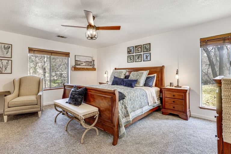 Spacious master bedroom featuring a wooden sleigh bed, patterned bedding, and a ceiling fan over plush carpet.