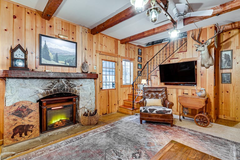 Cozy lodge-style living room featuring a stone fireplace, wood panel walls, and a leather armchair.
