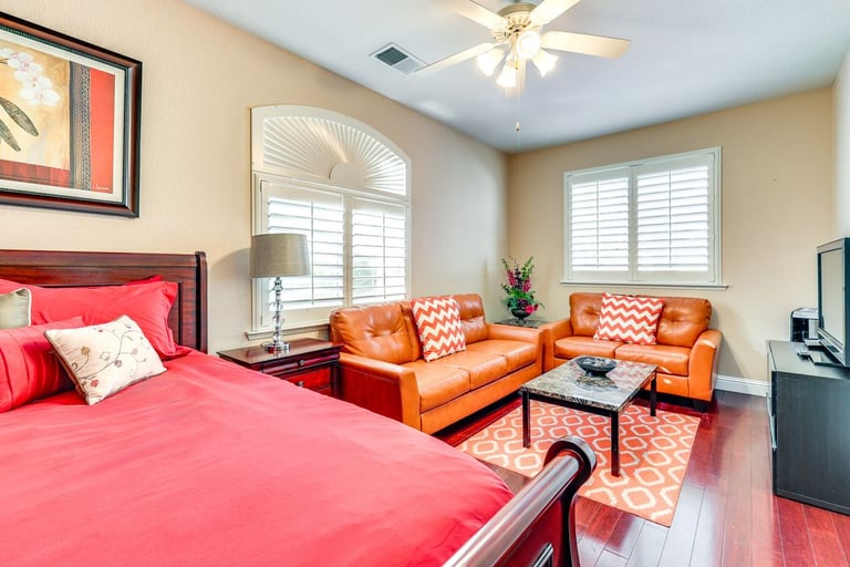 Modern bedroom with red bedding, leather sofas, and a marble coffee table on red hardwood floors.