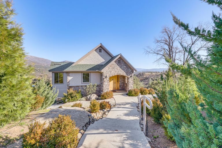 Luxury mountain home with stone exterior and concrete walkway surrounded by evergreen trees.