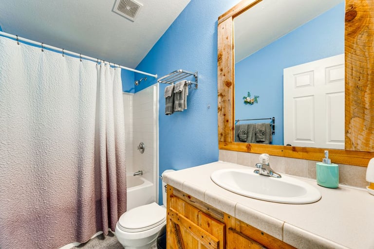 A bright blue bathroom with rustic wooden vanity and white tiled shower-tub combo.