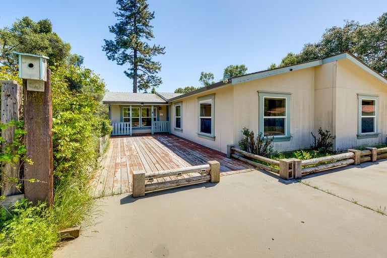 A light yellow ranch-style house featuring a rustic wooden deck and birdhouse in a sunny yard.