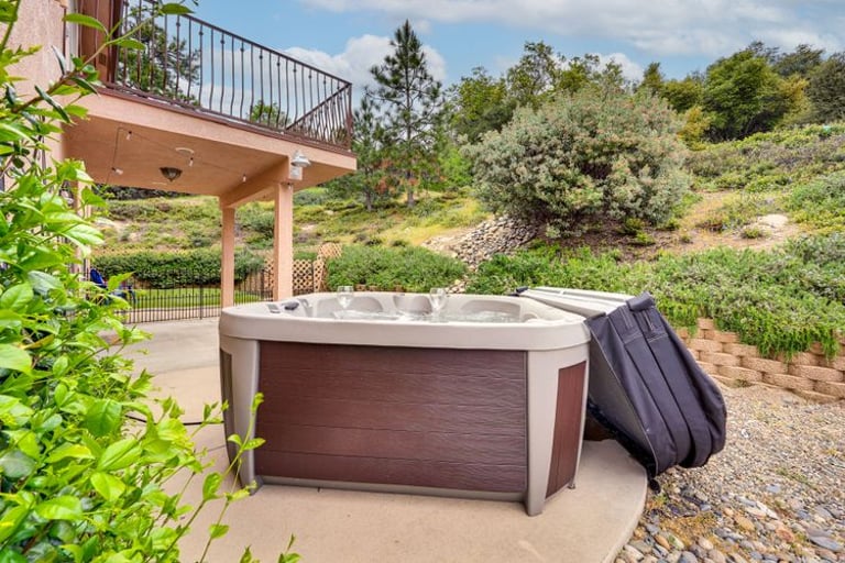 Outdoor luxury hot tub on a concrete patio overlooking a lush green hillside landscape.