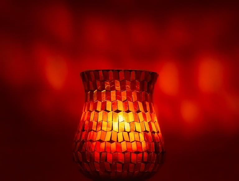 Glowing red mosaic glass candle holder with warm orange light against a bokeh background.