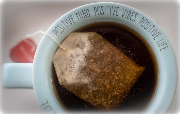 A tea bag steeping in a light blue ceramic mug featuring a motivational positive vibes quote.