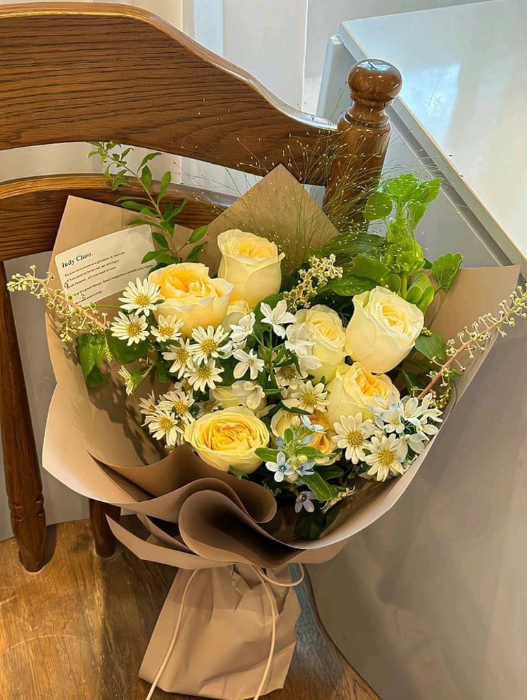 ramo de rosas amarillas con follaje verde margaritas color blanco envueltas en papel cafe 