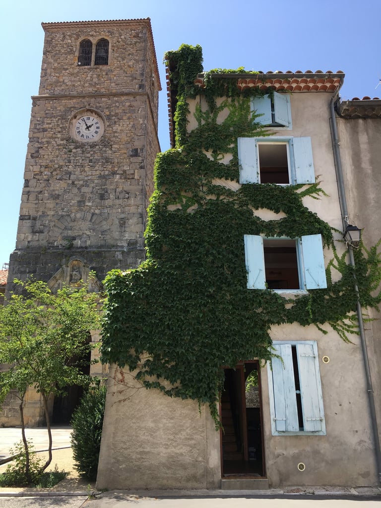 Historic stone clock tower next to an ivy-covered Quillan village house with light blue shutters.