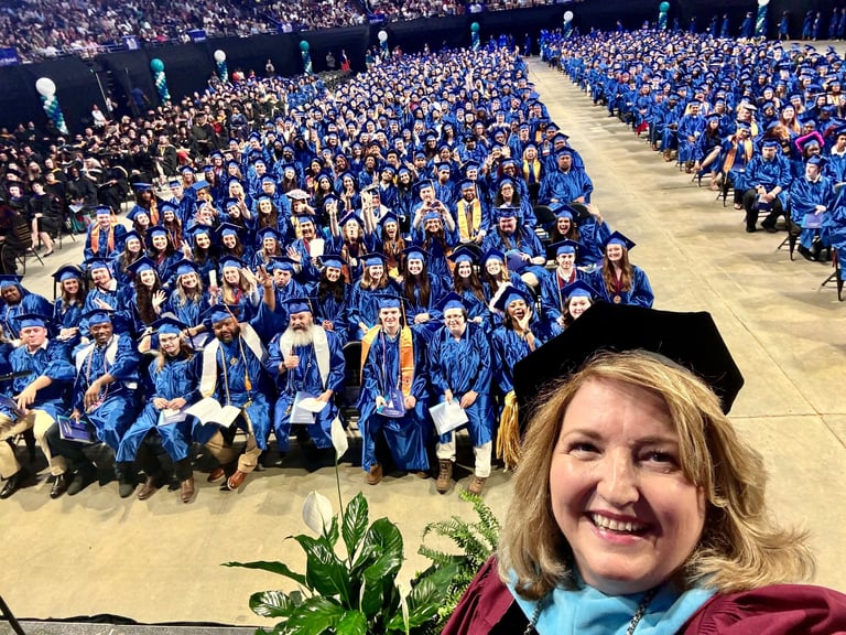 A graduation ceremony at a community college with students and president taking a selfie.