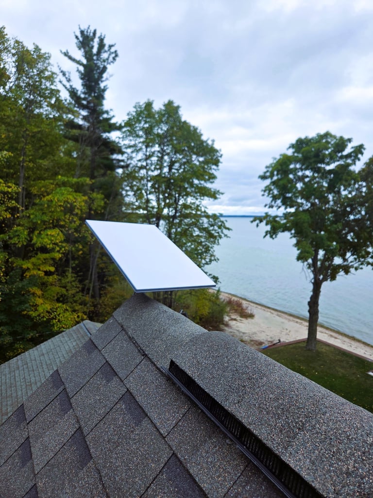 Rooftop Starlink dish overlooking lakefront property with trees, beach, and water.