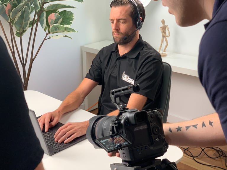 man with headset working on laptop while someone with camera films