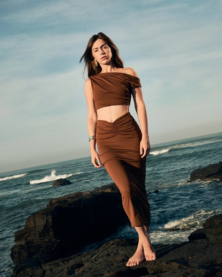 Fashion model walking on Bali's rocky volcanic coastline in earth tones.