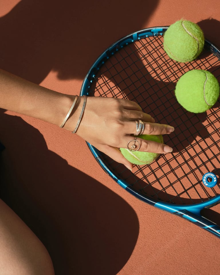 Tennis racket with green balls and rings, sports jewelry campaign shot.