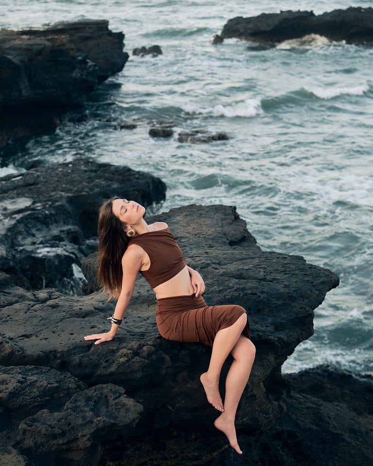Fashion model reclining on volcanic rocks in golden light, coastline shoot.