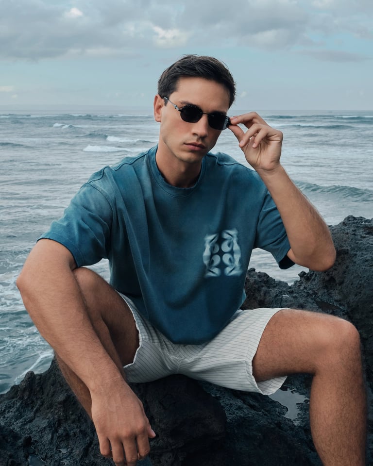 Male model in blue oversized T-shirt sitting on volcanic rocks for Break the Cycle Summer 2025 Bali.