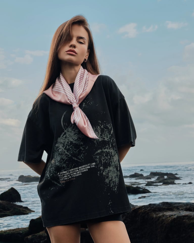 Female model in black oversized tee and pink scarf on volcanic rocks for Break the Cycle Summer 2025.