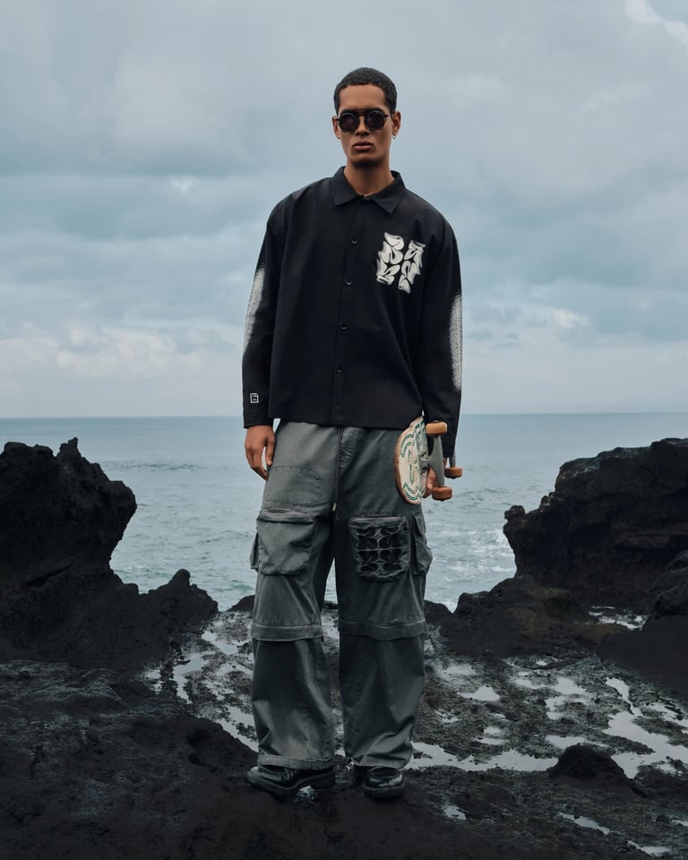 Male model in black shirt holding skateboard on volcanic rocks for Break the Cycle Summer 2025.
