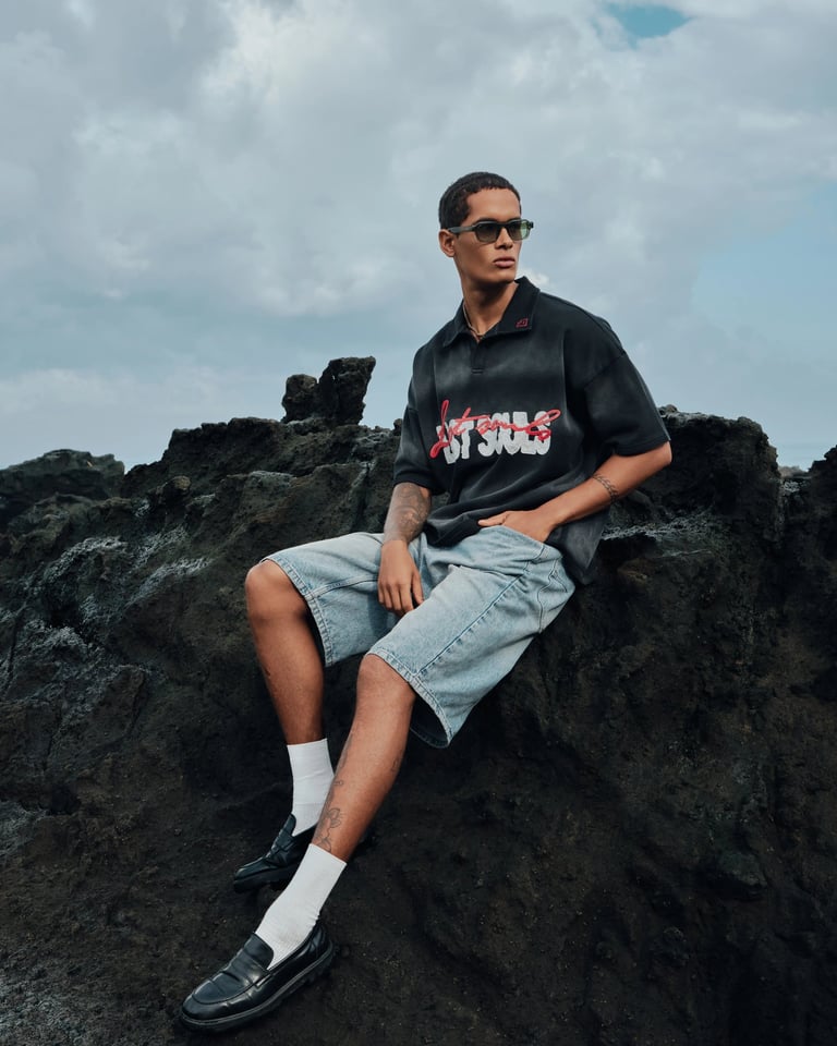 Male model in striped oversized tee sitting on rocks for Break the Cycle Summer 2025 Bali.