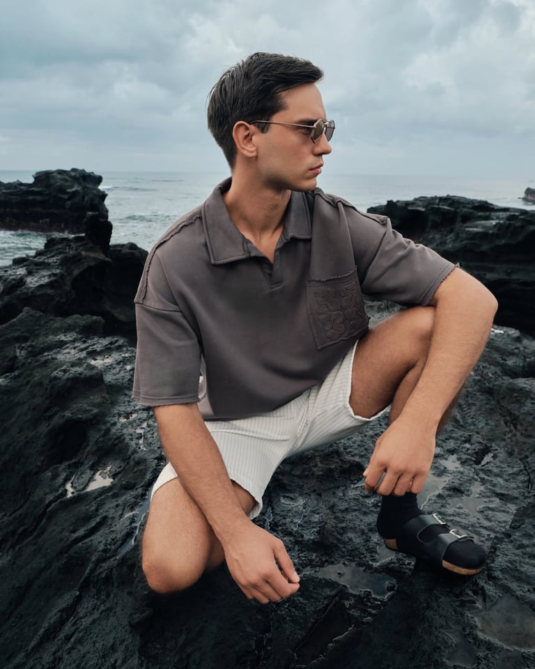 Male model in light brown streetwear squatting on Bali rocks for Break the Cycle Summer 2025.