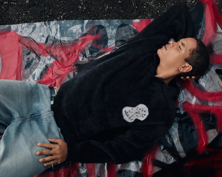 Male model in black sweater lying on top of Break the Cycle signage for summer campaign Bali 2025.