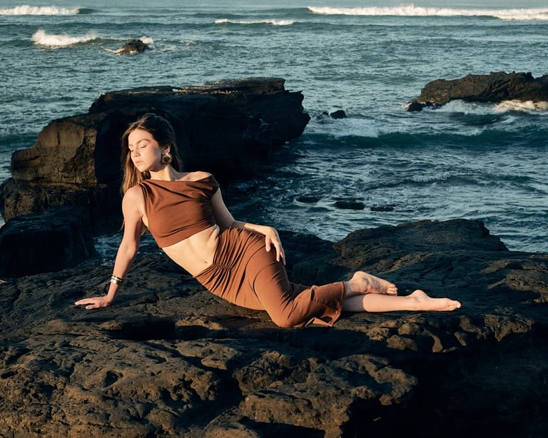 Model leaning against textured volcanic stones, Kini Produksi fashion portrait.