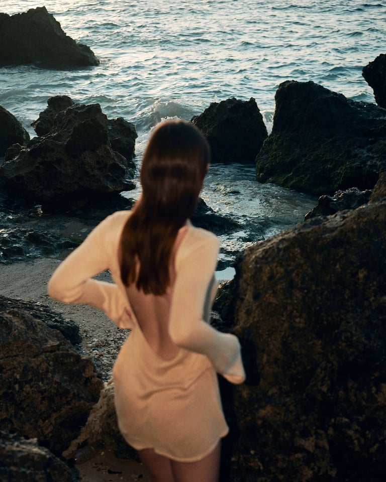 Back view of model in sheer dress on volcanic coastline path, Bali.