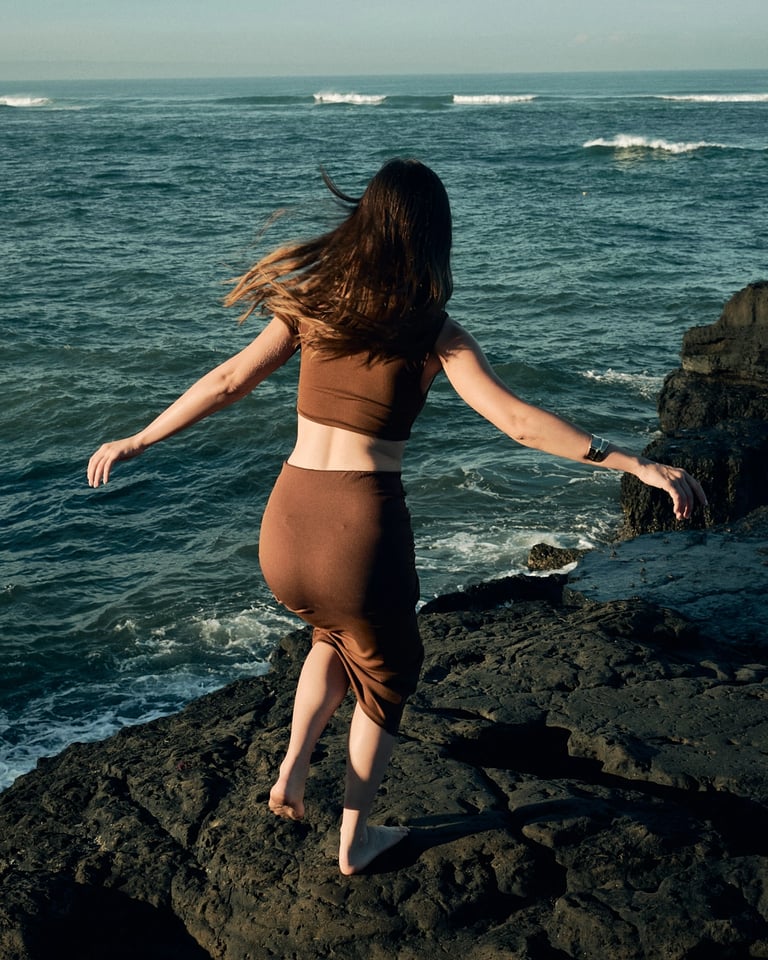 Side profile of model stepping across volcanic cliff edge, Bali editorial.