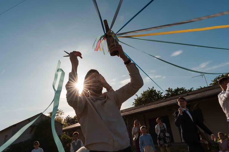Des invités brandissent des rubans colorés lors d'une célébration de mariage en plein air, baignée de soleil.