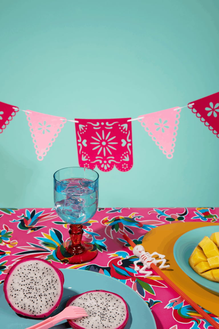 Festiva mesa de celebración mexicana con fruta del dragón, pancarta picado y un cóctel azul helado.