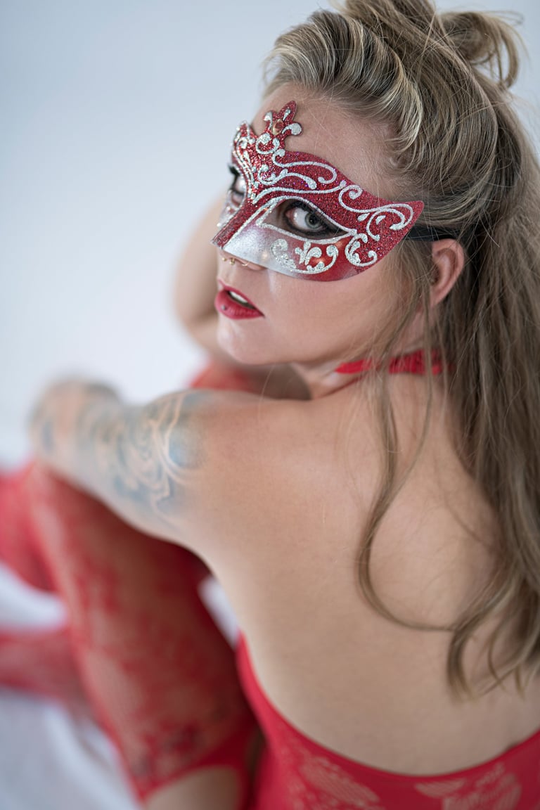 Boudoir-Portrait einer Frau mit kunstvoller rot-silberner Maske und roter Spitzenkleidung, aufgenommen im ästhetischen Finear