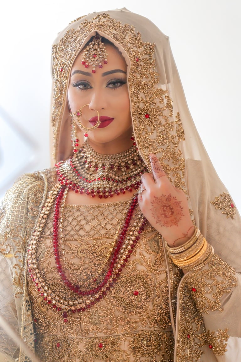 reflection of asian bride in traditional gold dress and jewellery  looking in mirror, and at camera lens, blurry background 