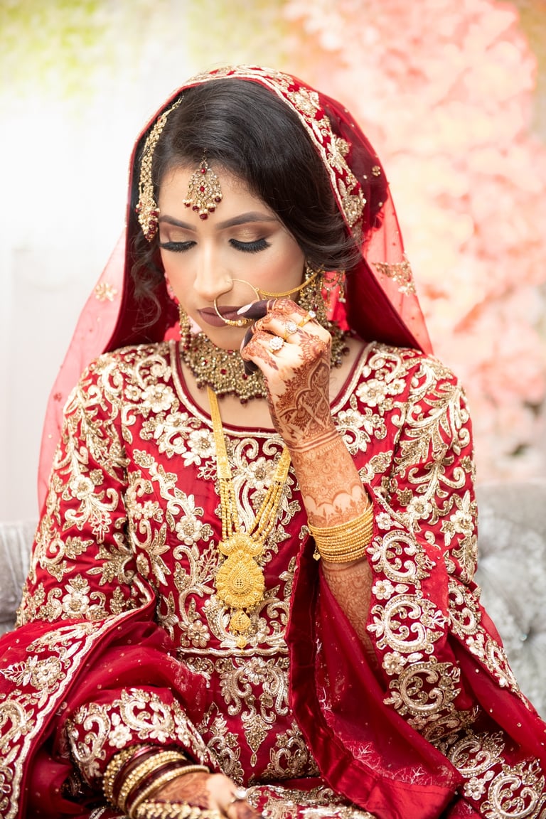 candid portrait of asian bride wearing traditional red dress with gold embroidery, her hands full of henna, looking down