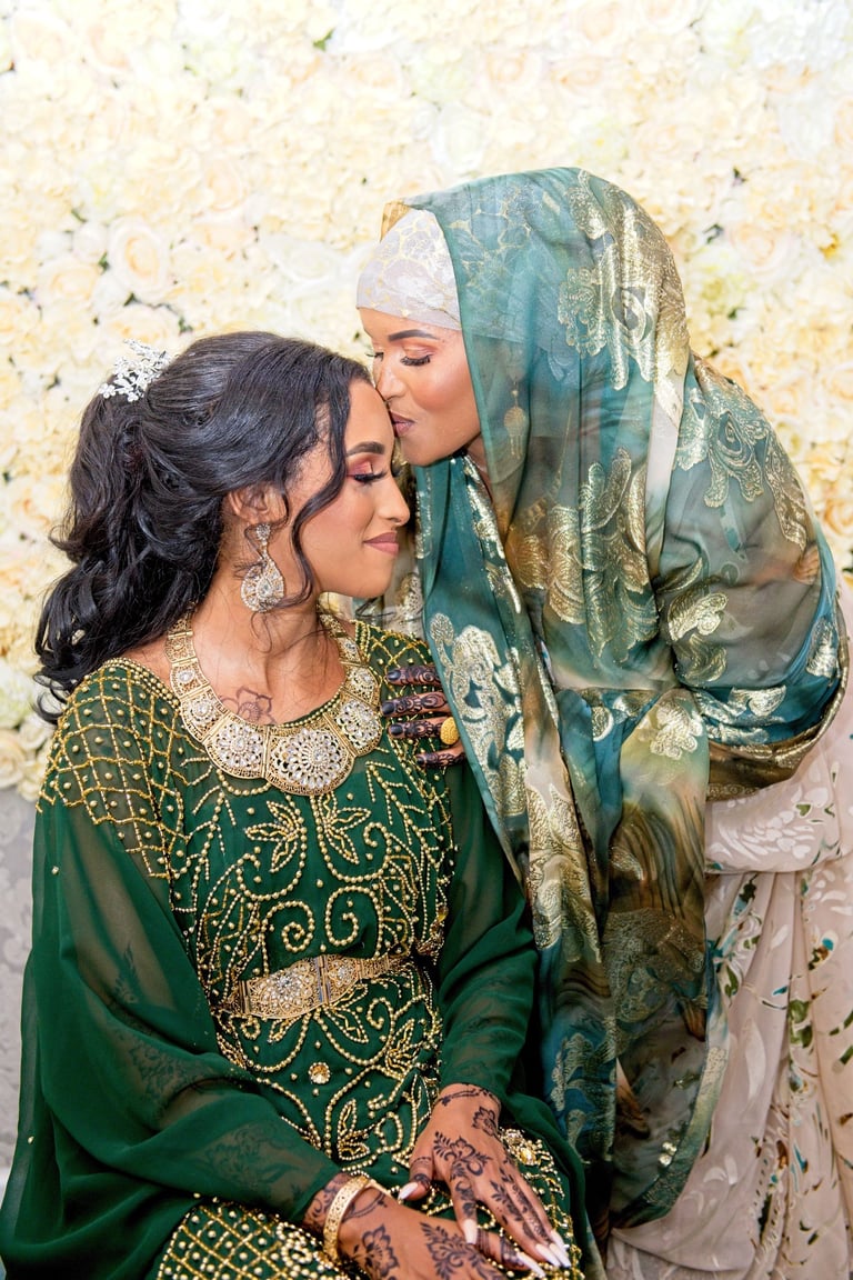 Somalian bride being kissed by mum, candid photo both smiling and both in traditional green outfits 