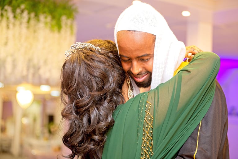 Somalian bride and groom hugging, bride's arm framing groom's face, back of bride's body and front of groom's face shown