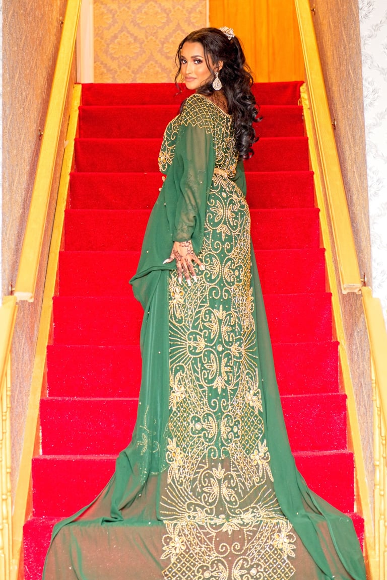 full length photo of Somalian bride wearing green traditional dress with gold beads standing on red staircase, bride smiling