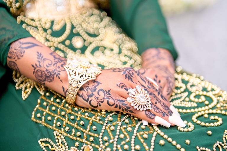 close up photo of bride's hands with henna, her green traditional dress with gold beads is blurred out and is the backdrop