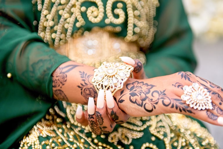 close up photo of bride putting on bracelet, her green traditional dress with gold beads is blurred out and is the backdrop