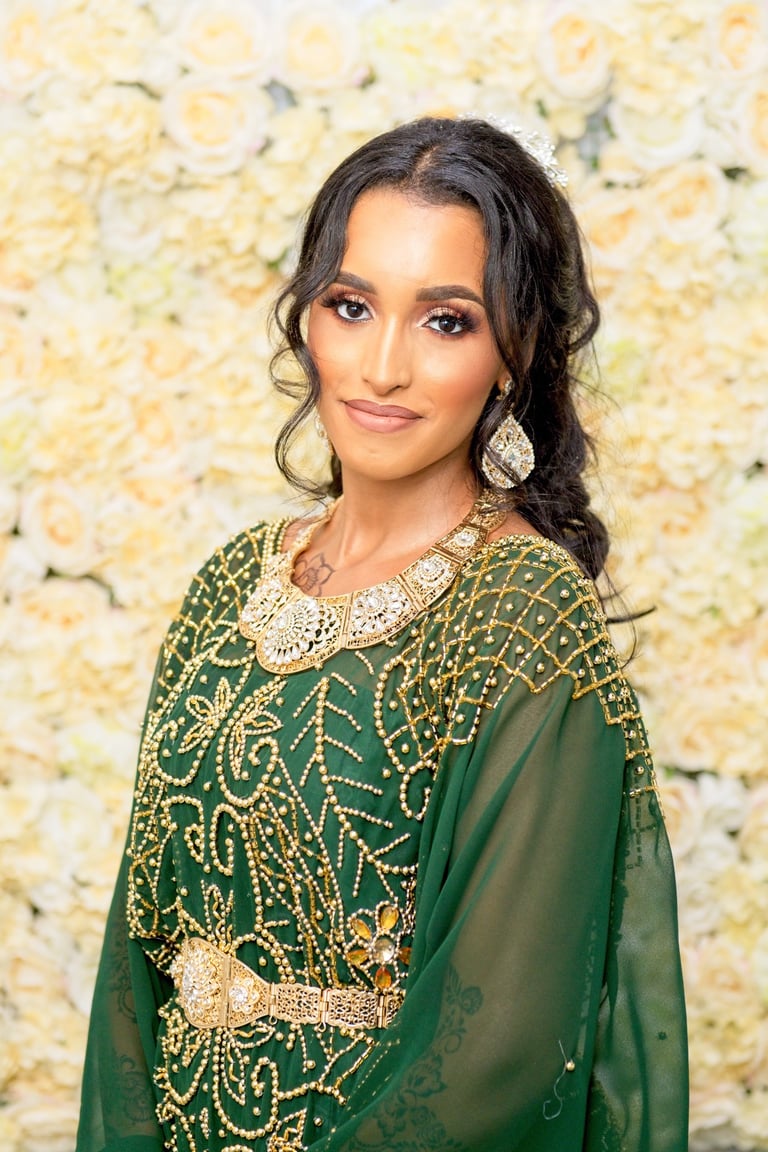 Somalian bride dressed in traditional dress and gold beaded dress with traditional gold jewellery looking at camera & smiling