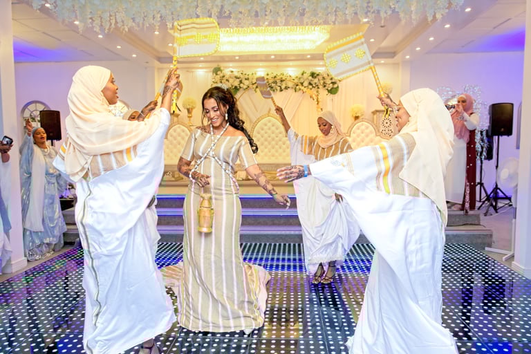 Happy Somalian bride dancing with bridesmaids, all happy, all dressed in traditional white & gold dresses