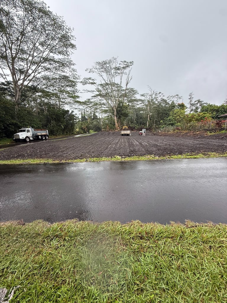White dump truck and heavy excavation machinery leveling a dirt construction site near a paved road.