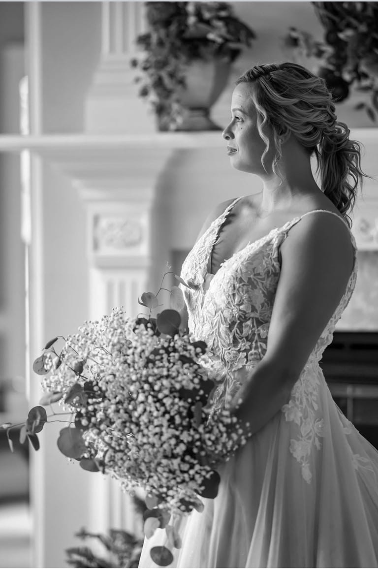 Black and white portrait of bride in lace gown with wavy ponytail hairstyle, holding bouquet of baby's breath and eucalyptus.