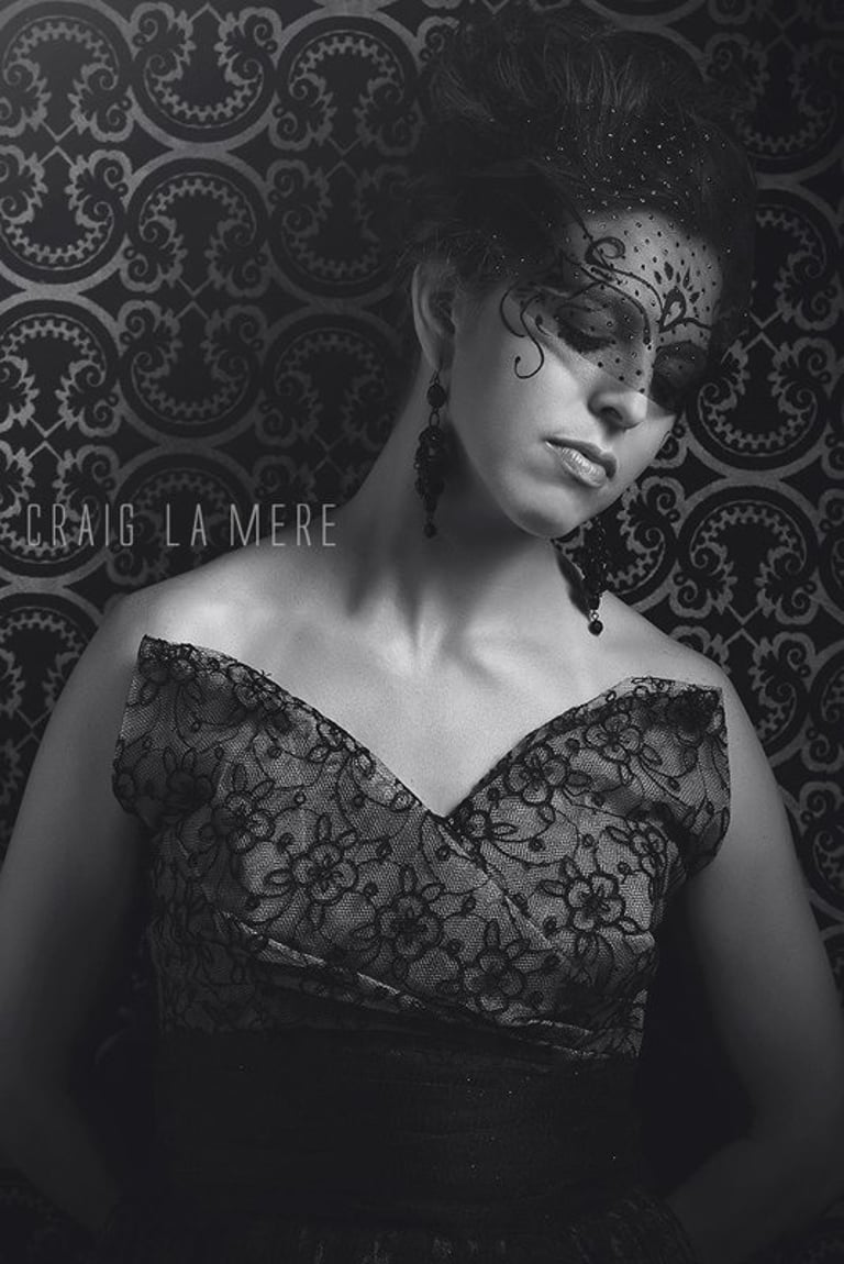Black and white portrait of woman in lace dress with dramatic updo, lace face veil, bold makeup and statement earrings.