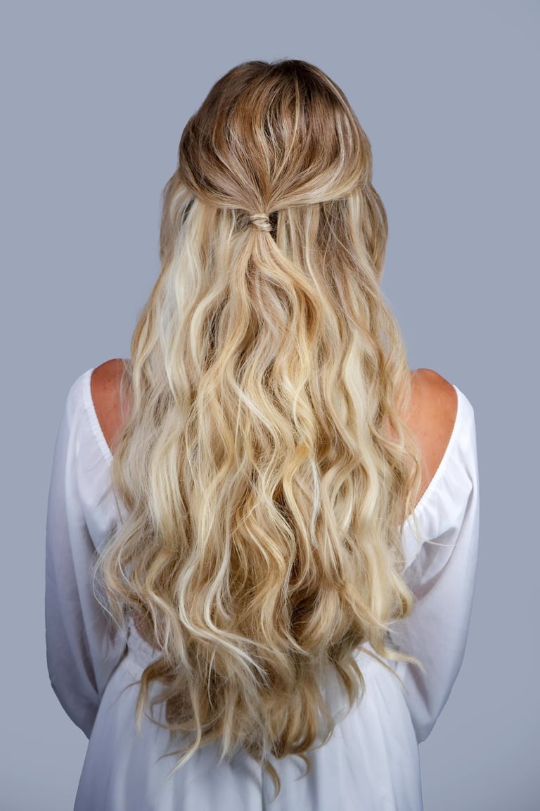 Bride with long blonde hair styled in half up half down waves with knot detail, simple romantic hairstyle for wedding day.
