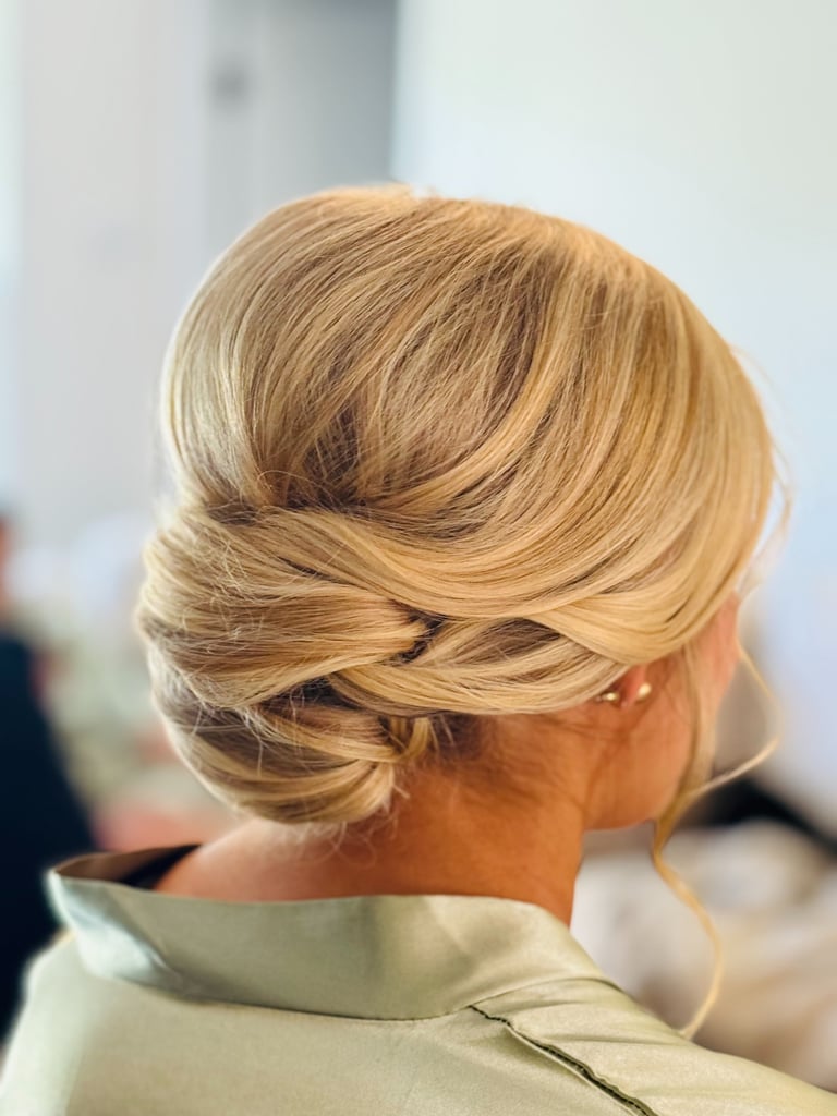 Blonde bride with smooth low twist updo hairstyle and soft face framing pieces, elegant timeless look for wedding day style.