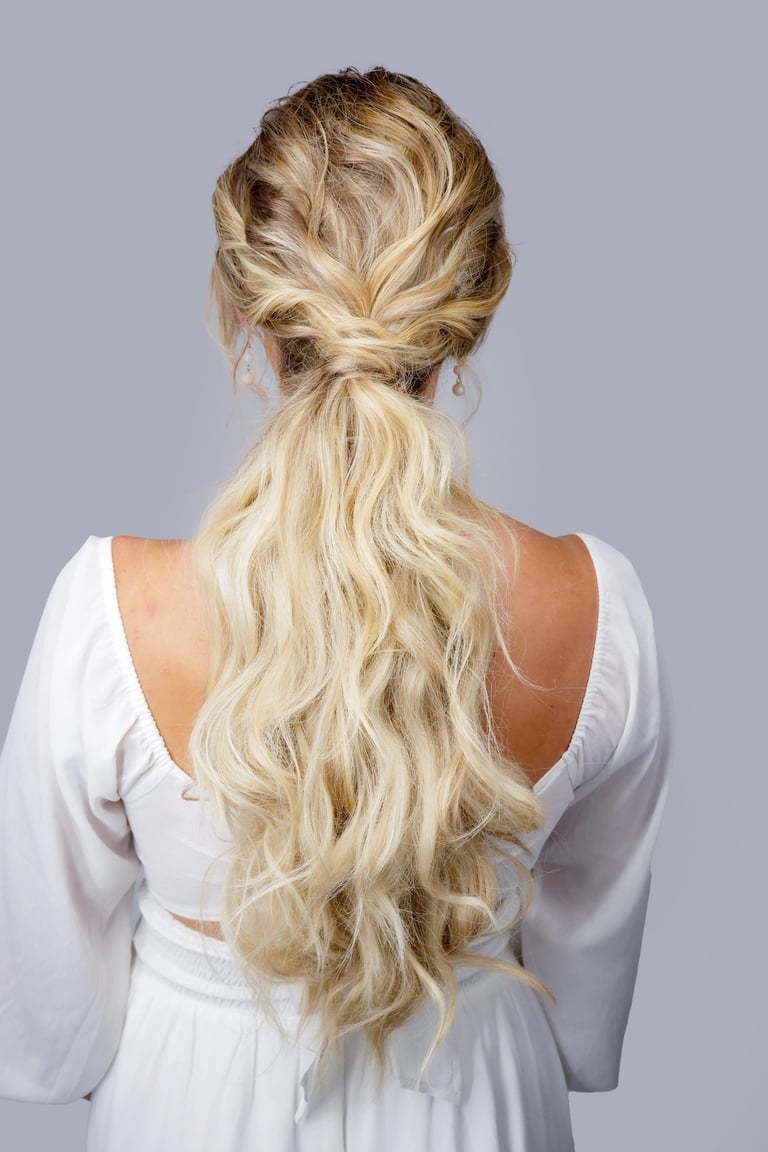 Bride with blonde hair styled in textured low ponytail with loose waves, romantic boho hairstyle for wedding day look.