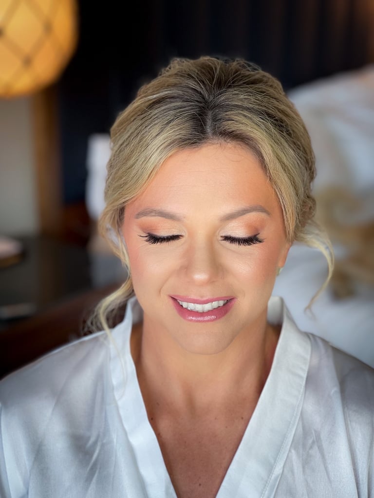 Bride with blonde hair in an elegant updo, soft-glam wedding makeup, long lashes, neutral eyeshadow, and glossy pink lips.