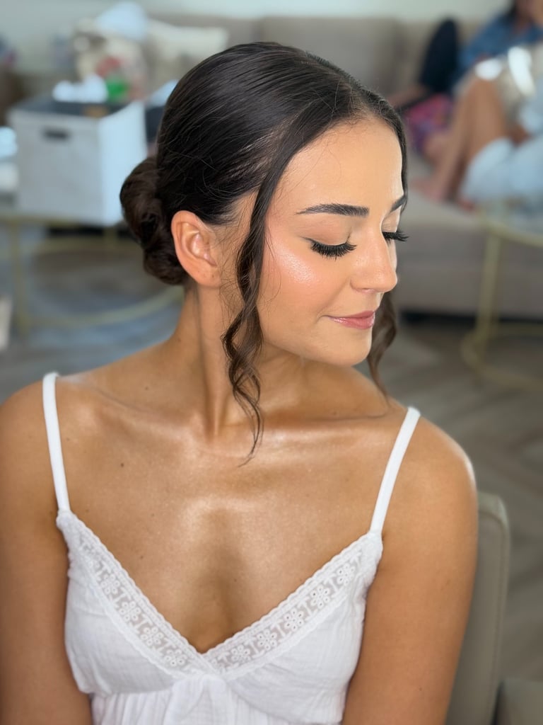 Bride with soft-glam wedding makeup, winged eyeliner, rosy lips, glowing skin, and hair styled in a low bun with loose curls.